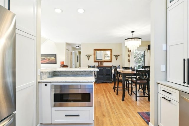 kitchen featuring an inviting chandelier, light wood finished floors, white cabinets, and stainless steel appliances