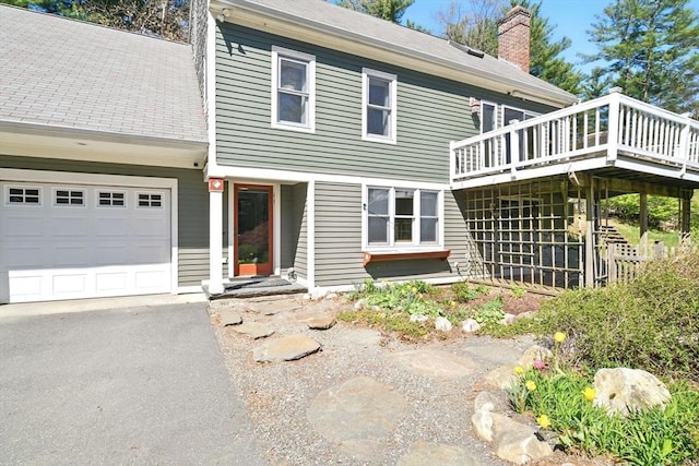 exterior space featuring an attached garage, driveway, a wooden deck, and a chimney