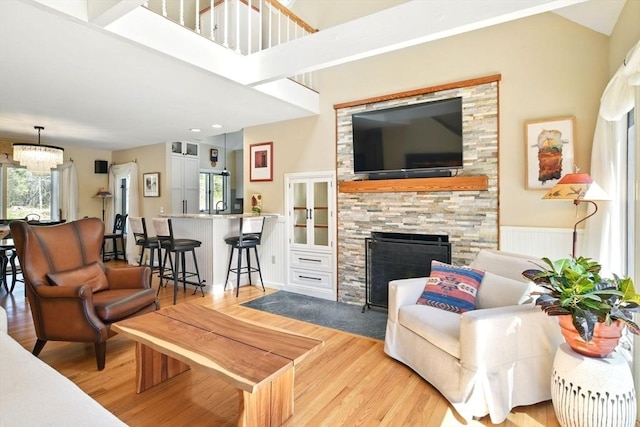 living room featuring plenty of natural light, wood finished floors, a chandelier, and a stone fireplace