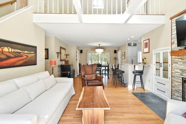living room featuring recessed lighting, a fireplace, light wood finished floors, and a towering ceiling