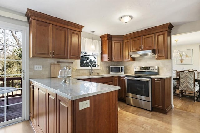 kitchen featuring light wood finished floors, a healthy amount of sunlight, under cabinet range hood, appliances with stainless steel finishes, and a peninsula