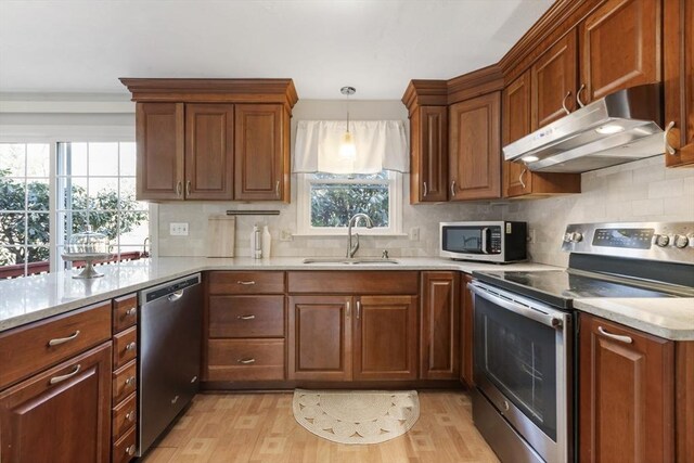 kitchen featuring light wood-style flooring, a sink, decorative backsplash, appliances with stainless steel finishes, and under cabinet range hood