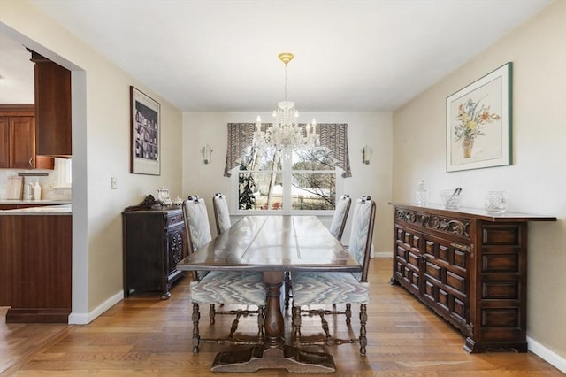 dining room with light wood-type flooring, baseboards, and an inviting chandelier