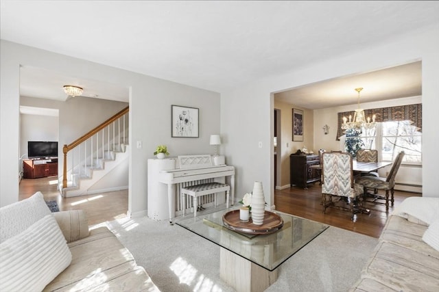 living room featuring a baseboard heating unit, baseboards, stairs, wood finished floors, and a notable chandelier