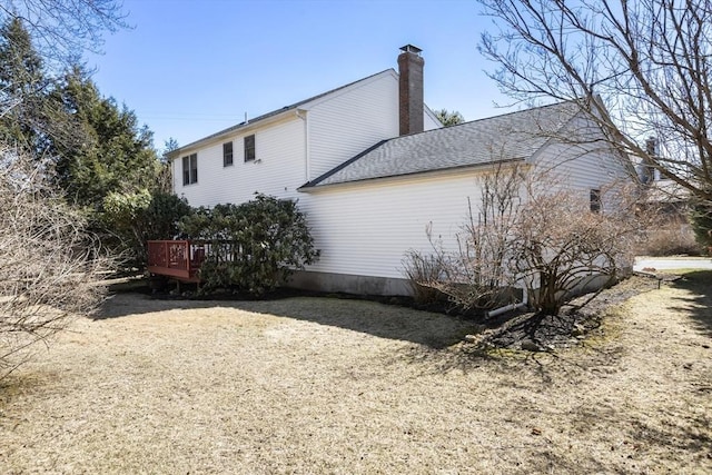 view of home's exterior with roof with shingles, a deck, and a chimney