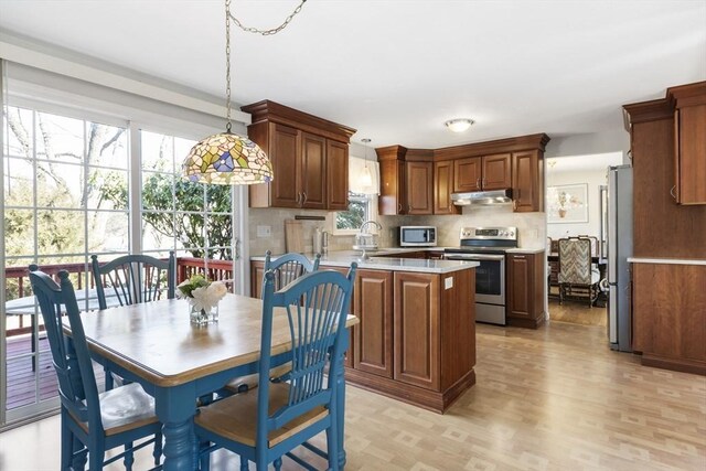 kitchen with under cabinet range hood, appliances with stainless steel finishes, a peninsula, light countertops, and decorative backsplash