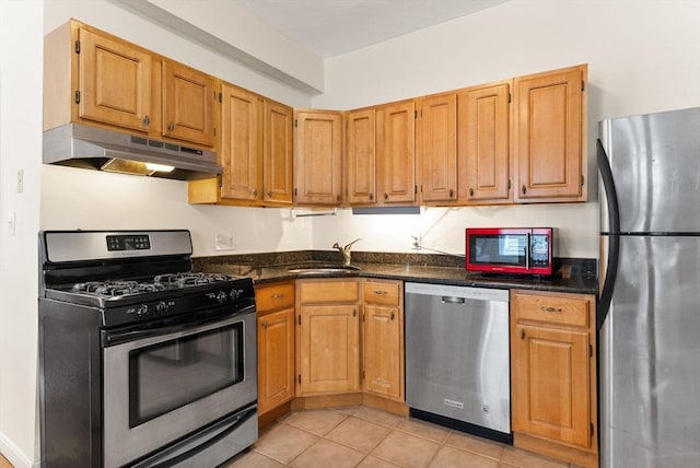 kitchen with dark stone countertops, sink, light tile patterned floors, and stainless steel appliances