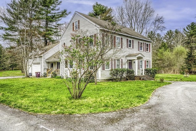 colonial home featuring a shingled roof, a front lawn, and an attached garage