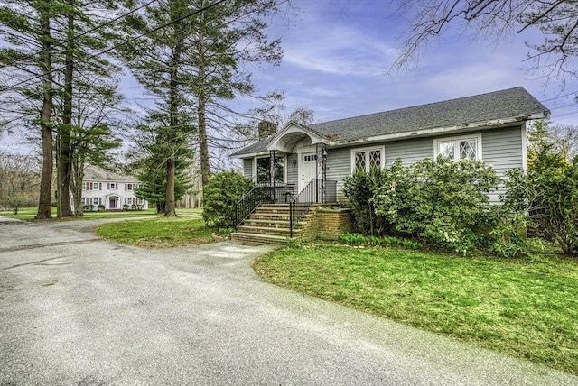 single story home with aphalt driveway, roof with shingles, a chimney, and a front yard