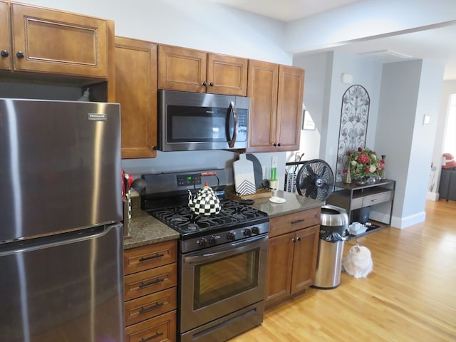 kitchen featuring dark stone counters, light wood-type flooring, and appliances with stainless steel finishes