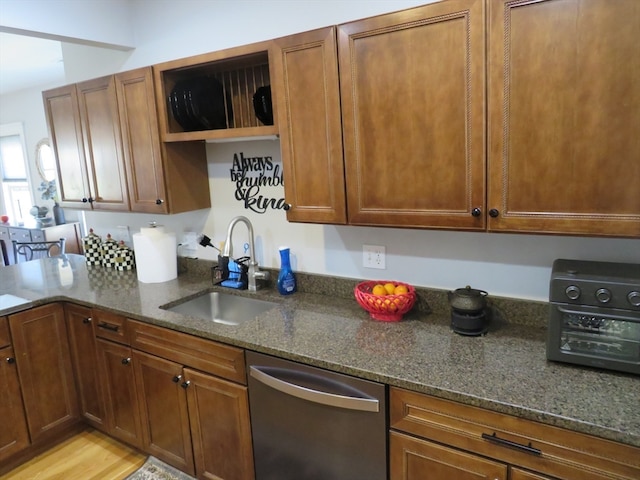 kitchen with light hardwood / wood-style floors, stainless steel dishwasher, dark stone countertops, and sink