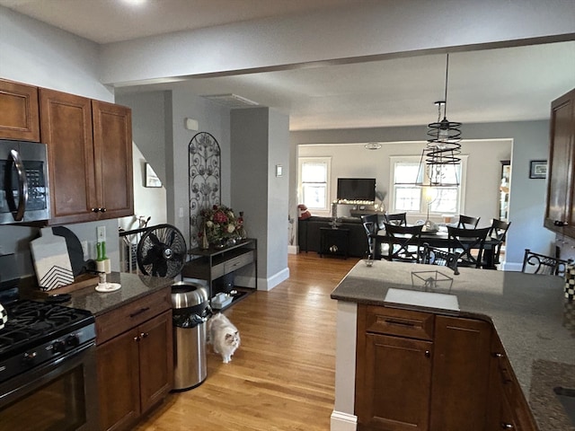 kitchen featuring black range, light hardwood / wood-style floors, dark stone countertops, and hanging light fixtures