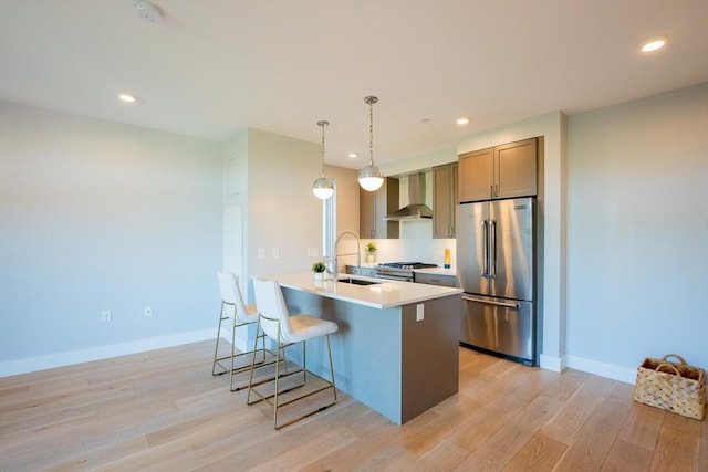 kitchen with wall chimney exhaust hood, a breakfast bar, sink, decorative light fixtures, and appliances with stainless steel finishes