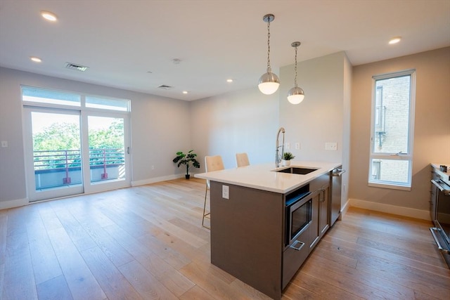 kitchen with sink, light hardwood / wood-style flooring, a breakfast bar, stainless steel appliances, and an island with sink