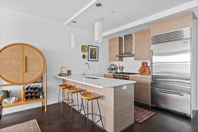 kitchen featuring a breakfast bar area, wall chimney exhaust hood, appliances with stainless steel finishes, kitchen peninsula, and sink