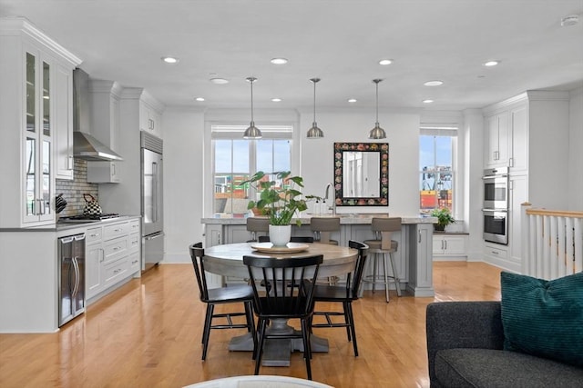 kitchen featuring wine cooler, a breakfast bar, stainless steel appliances, light wood-style floors, and wall chimney exhaust hood