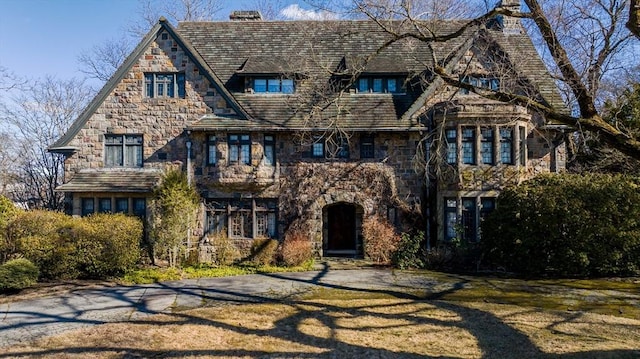 tudor-style house featuring stone siding, a chimney, and a front yard