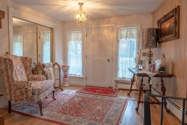 foyer with baseboard heating, a chandelier, a textured ceiling, and light wood-type flooring