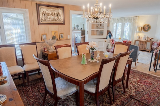 dining area with wood walls, hardwood / wood-style floors, a healthy amount of sunlight, and a notable chandelier