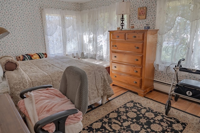 bedroom with multiple windows, light hardwood / wood-style floors, and a baseboard radiator