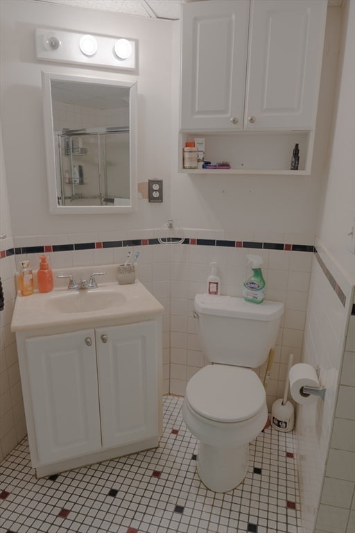 bathroom with an enclosed shower, vanity, tile walls, tile patterned flooring, and toilet