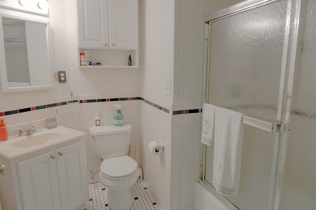 full bathroom with tile patterned floors, bath / shower combo with glass door, toilet, vanity, and tile walls