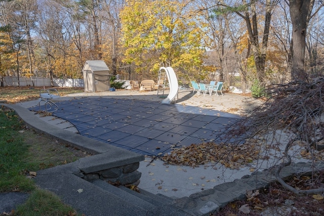 view of swimming pool with a storage shed, a patio area, and a water slide