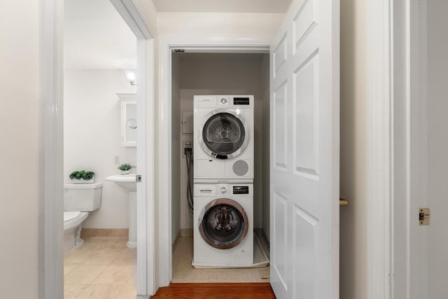 clothes washing area featuring stacked washing machine and dryer, light tile patterned floors, and baseboards