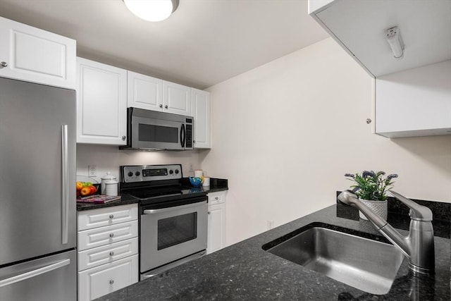 kitchen with stainless steel appliances, a sink, white cabinetry, and dark stone countertops