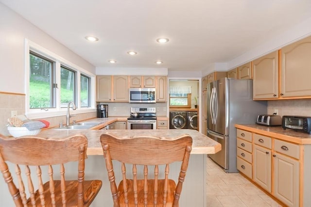 kitchen with a kitchen breakfast bar, separate washer and dryer, kitchen peninsula, and appliances with stainless steel finishes