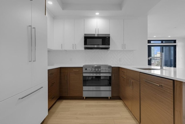 kitchen with light countertops, appliances with stainless steel finishes, white cabinetry, a sink, and light wood-type flooring