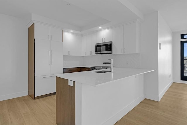 kitchen with paneled built in fridge, stainless steel microwave, a peninsula, light countertops, and white cabinetry