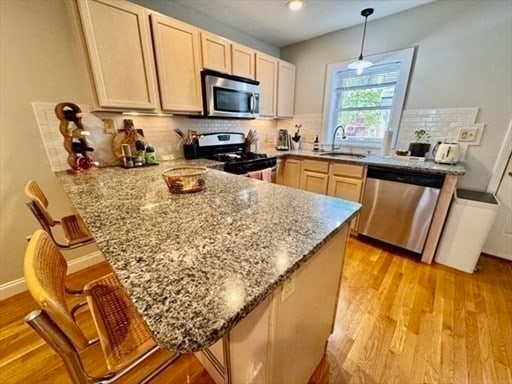 kitchen featuring kitchen peninsula, a breakfast bar area, light brown cabinets, and appliances with stainless steel finishes