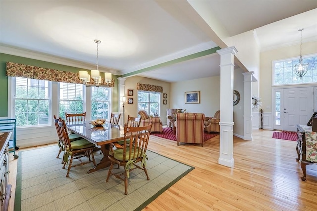 dining space featuring ornamental molding, light hardwood / wood-style floors, decorative columns, and a notable chandelier