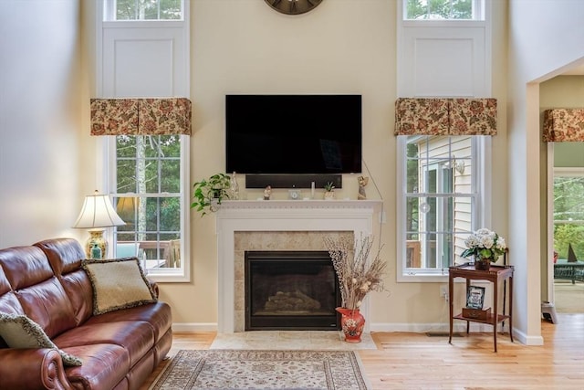 living room with a tiled fireplace, light hardwood / wood-style floors, and a high ceiling