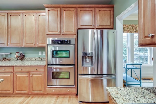 kitchen with light stone counters, light wood-type flooring, and appliances with stainless steel finishes