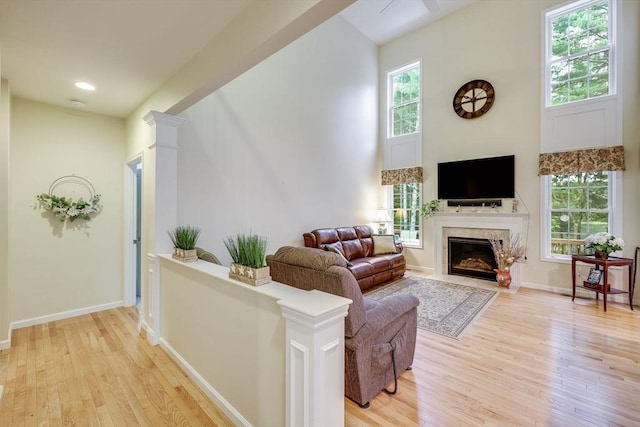 living room featuring decorative columns, a towering ceiling, a wealth of natural light, and light hardwood / wood-style flooring