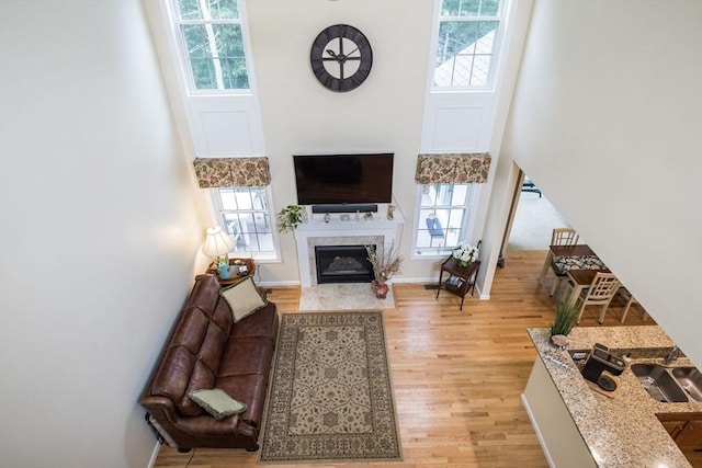 living room featuring a tiled fireplace, a towering ceiling, and light hardwood / wood-style flooring