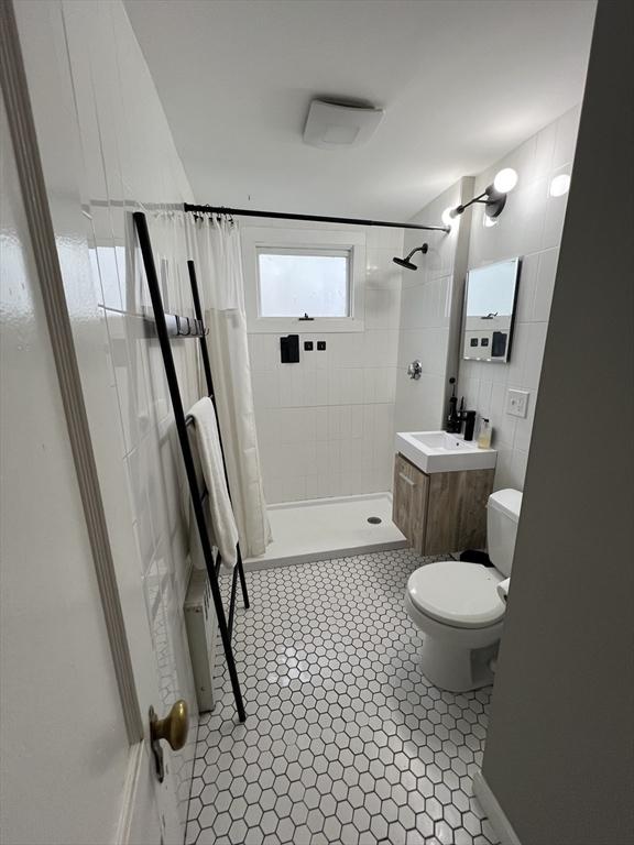 full bath featuring a stall shower, tile walls, toilet, tile patterned flooring, and vanity