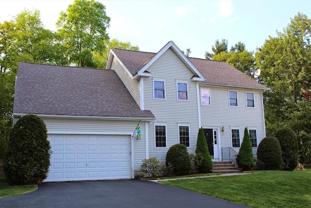 colonial house featuring aphalt driveway, a front yard, an attached garage, and a shingled roof