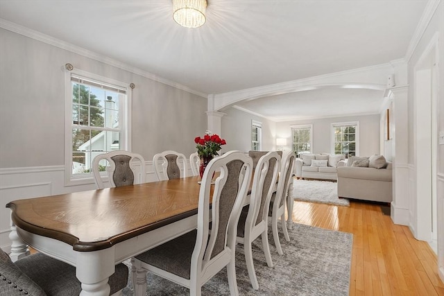 dining space featuring ornamental molding, a healthy amount of sunlight, a wainscoted wall, and light wood-type flooring