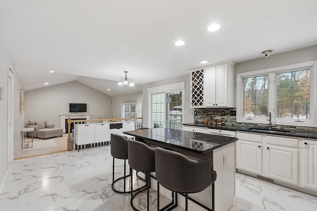 kitchen featuring lofted ceiling, a sink, marble finish floor, tasteful backsplash, and open floor plan