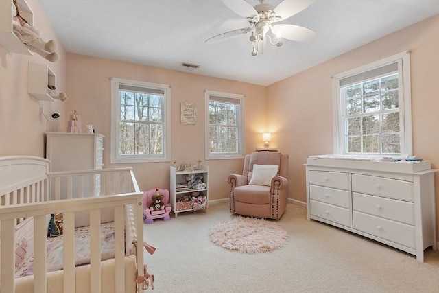 carpeted bedroom with baseboards, visible vents, a crib, and ceiling fan