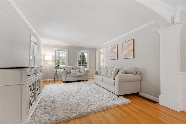 living room with arched walkways, light wood-style floors, crown molding, decorative columns, and baseboards