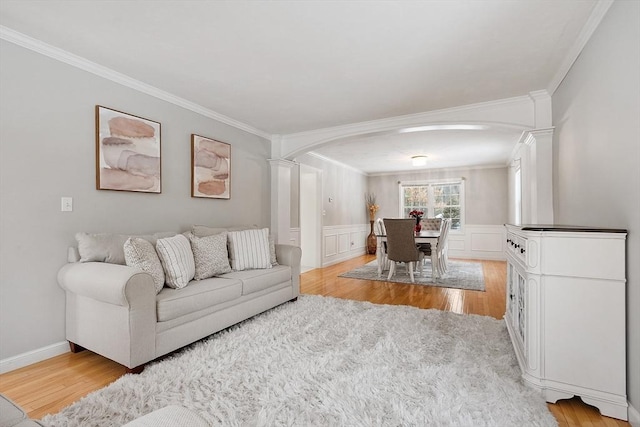 living area featuring a wainscoted wall, light wood-type flooring, ornamental molding, decorative columns, and arched walkways