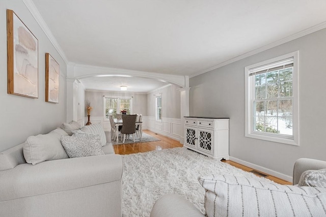 living area with a wainscoted wall, ornamental molding, and wood finished floors