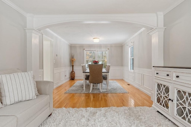 dining space with arched walkways, wood finished floors, crown molding, and decorative columns