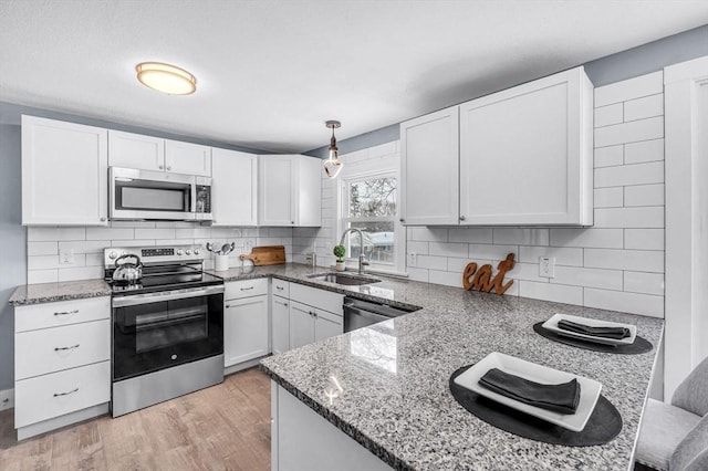 kitchen featuring tasteful backsplash, white cabinets, stainless steel appliances, pendant lighting, and a sink