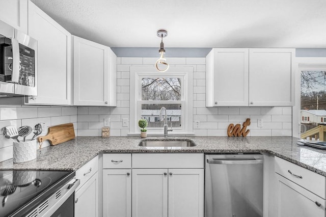 kitchen featuring tasteful backsplash, white cabinets, light stone countertops, stainless steel appliances, and a sink