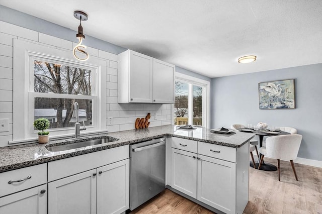 kitchen featuring dark stone counters, dishwasher, decorative light fixtures, a peninsula, and a sink